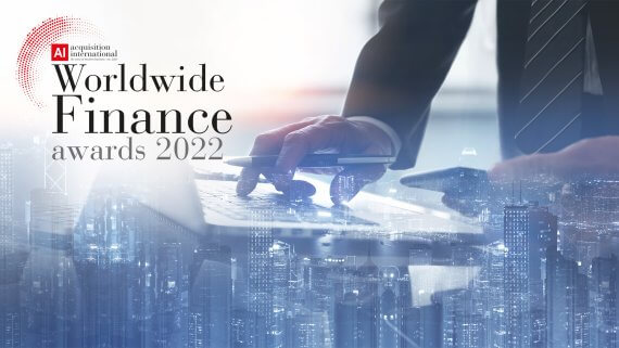 Double exposure image of a business man writing on a finance report, with a cityscape blended in. The 2022 Worldwide Finance Awards logo is in the top left corner