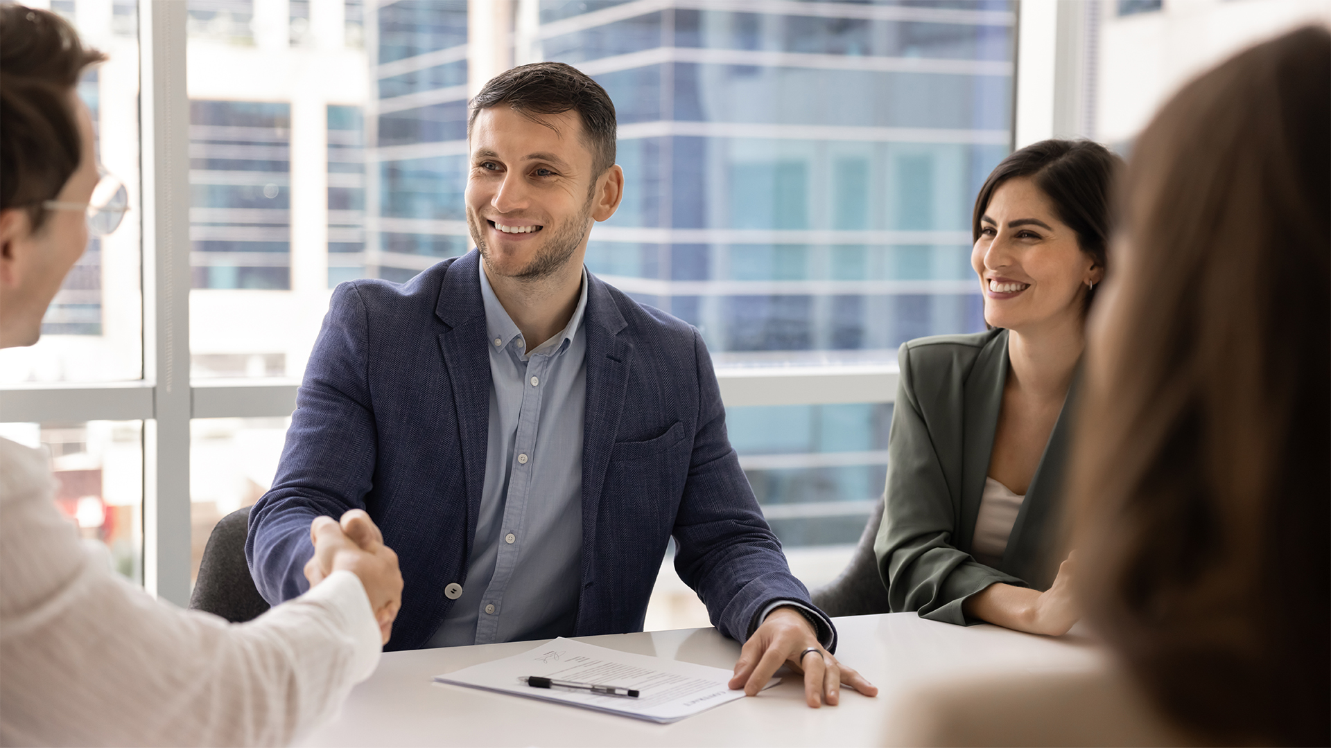 Company boss greets corporate client, investor or shareholder with handshake gesture, gathered together around table in board room